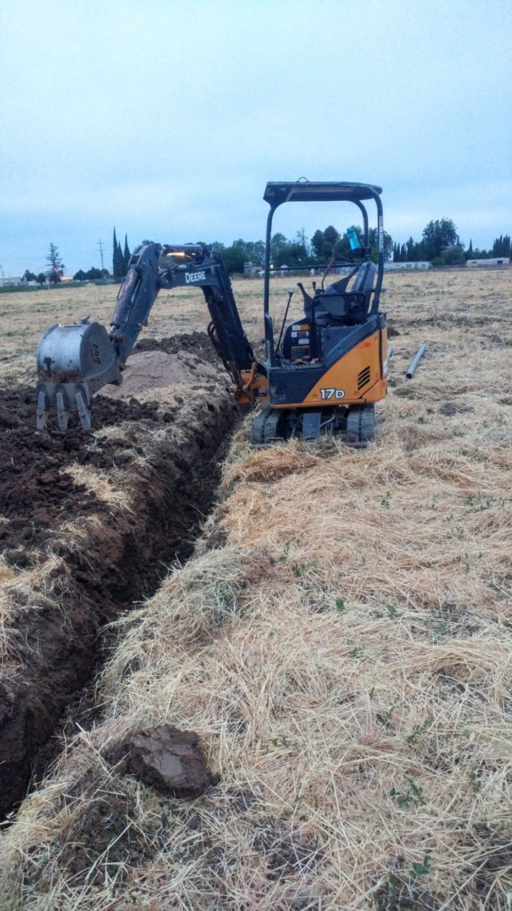 arm of excavator is turned sideways over an open trench