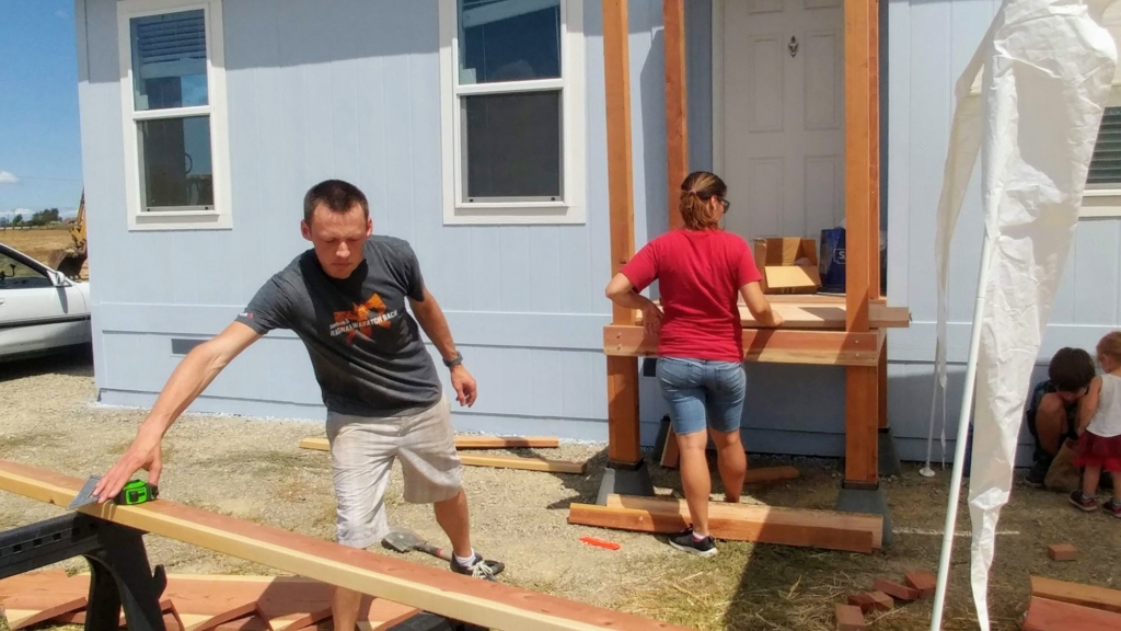 man grabbing green measuring tape as others build deck landing