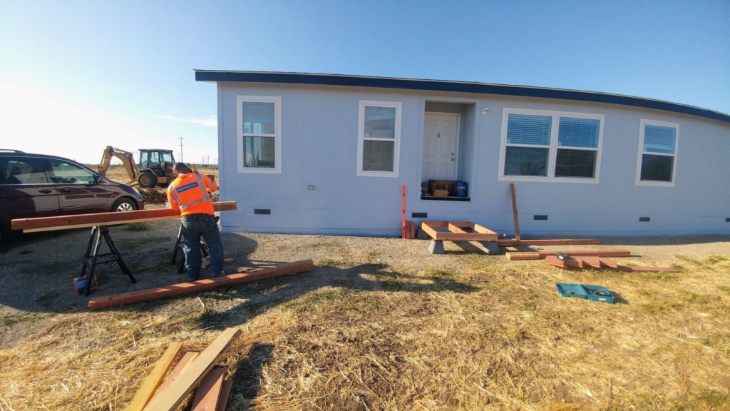 man cutting wood in front of manufactured home